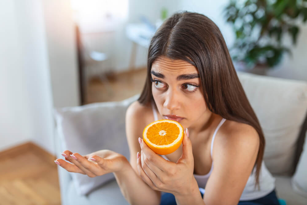 Sick woman trying to sense smell of half fresh orange