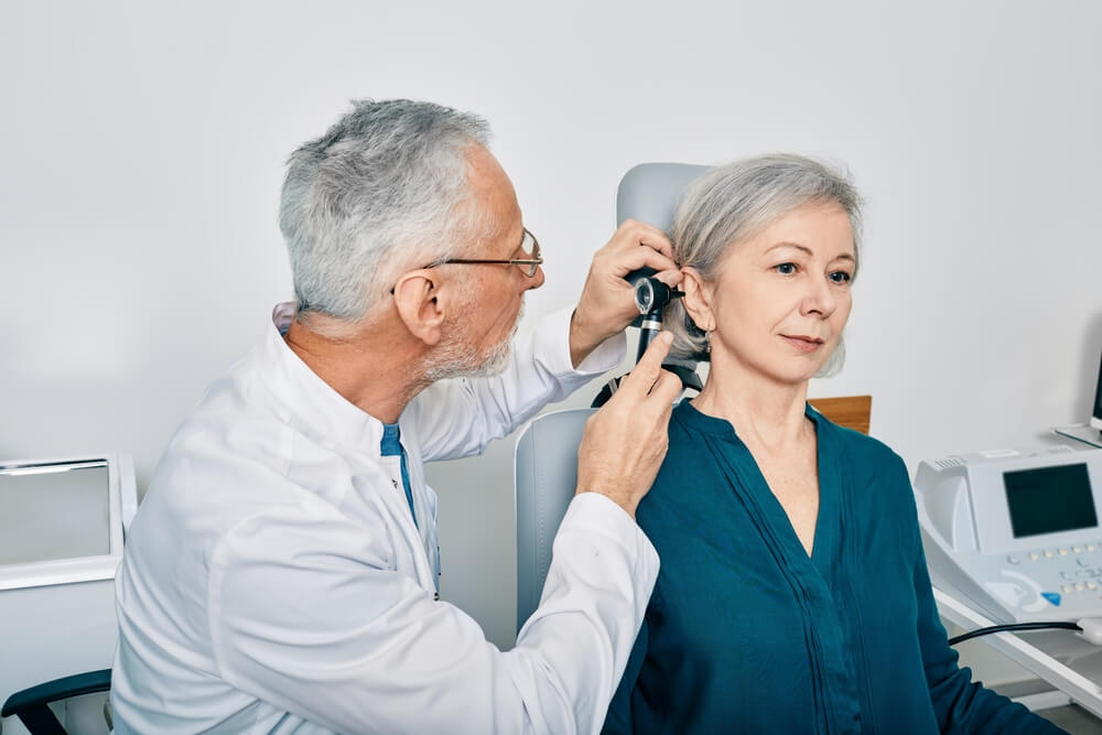 Otolaryngologist doctor checking senior woman's ear using otoscope or auriscope at hearing center. Audiology
