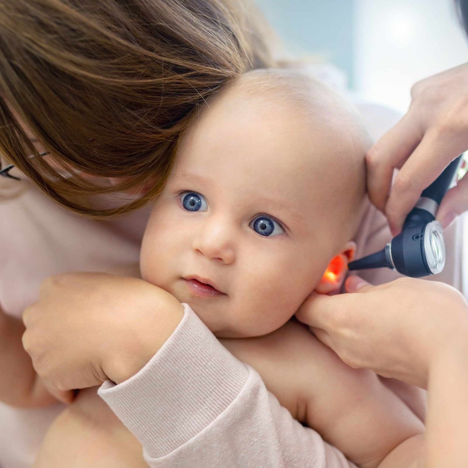 Doctor pediatrist examining childs ear with otoscope. Mom holding baby with hands